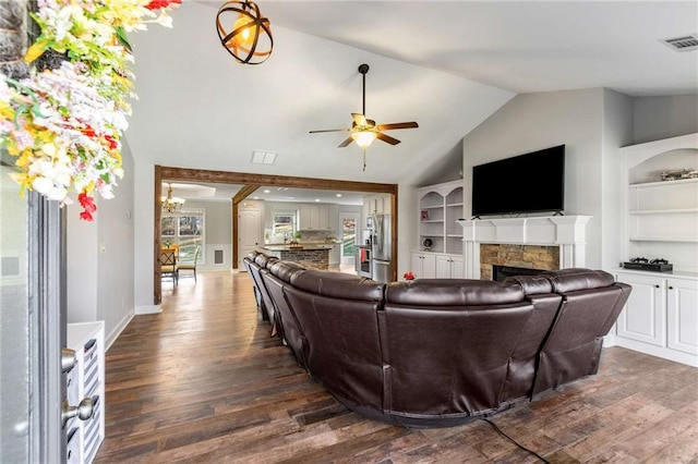 living room featuring visible vents, built in shelves, dark wood finished floors, a stone fireplace, and vaulted ceiling