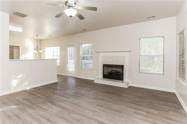 unfurnished living room with hardwood / wood-style floors, ceiling fan with notable chandelier, and a fireplace