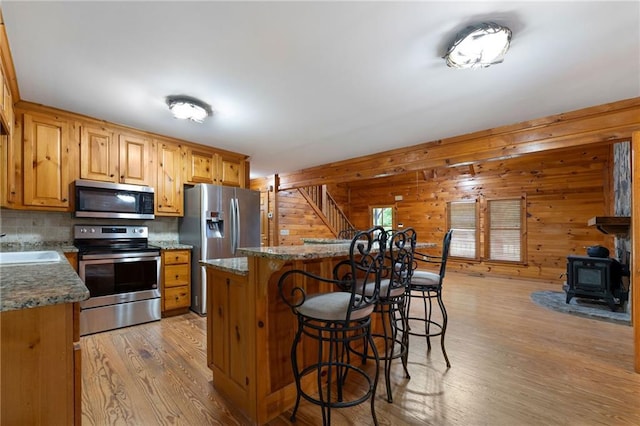 442 Cartecay River Run, Ellijay, GA 30536 - kitchen with appliances with stainless steel finishes, a kitchen breakfast bar, light wood-style floors, a wood stove, and decorative backsplash