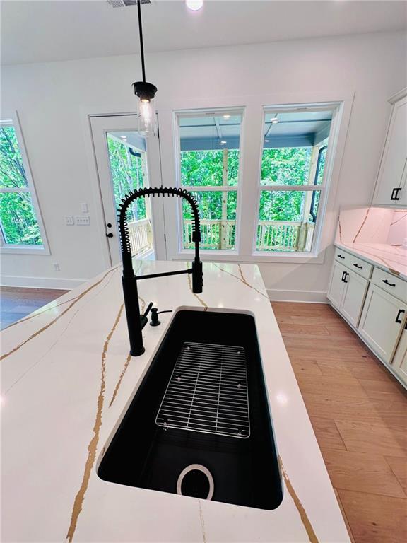 interior details featuring decorative light fixtures, white cabinets, light wood-style floors, and a sink