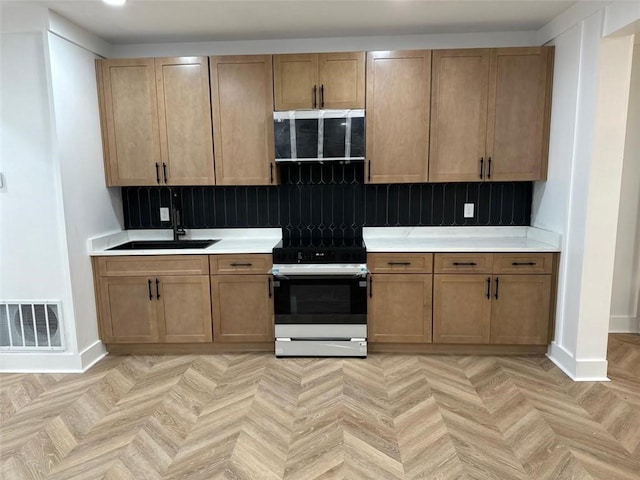 kitchen featuring visible vents, range with electric cooktop, a sink, light countertops, and baseboards