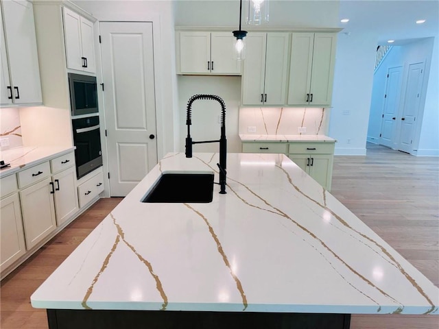 kitchen with light wood finished floors, wall oven, black microwave, and light stone counters