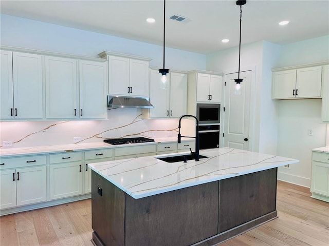 kitchen featuring under cabinet range hood, light wood finished floors, black appliances, and a sink