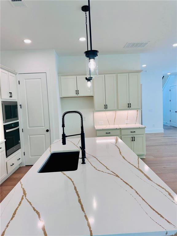 kitchen featuring decorative light fixtures, visible vents, light wood-style flooring, and a sink