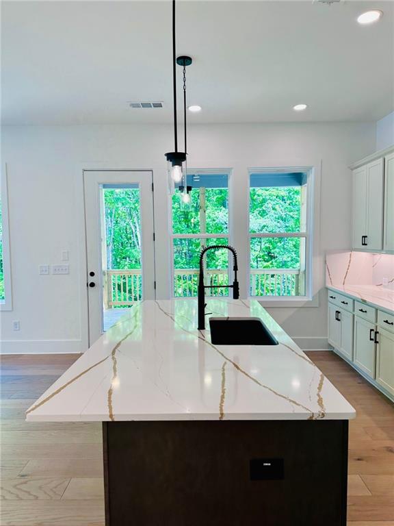 kitchen with a sink, light stone countertops, light wood-style floors, and a kitchen island with sink