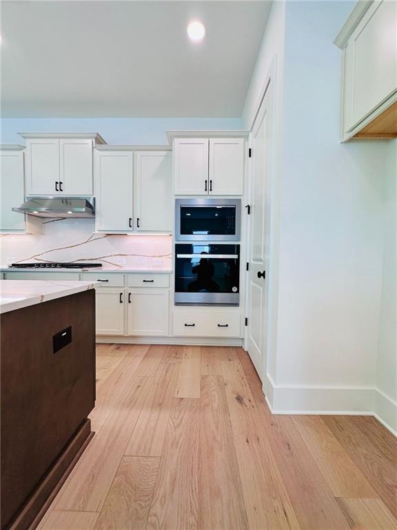 kitchen featuring under cabinet range hood, appliances with stainless steel finishes, light countertops, and light wood finished floors