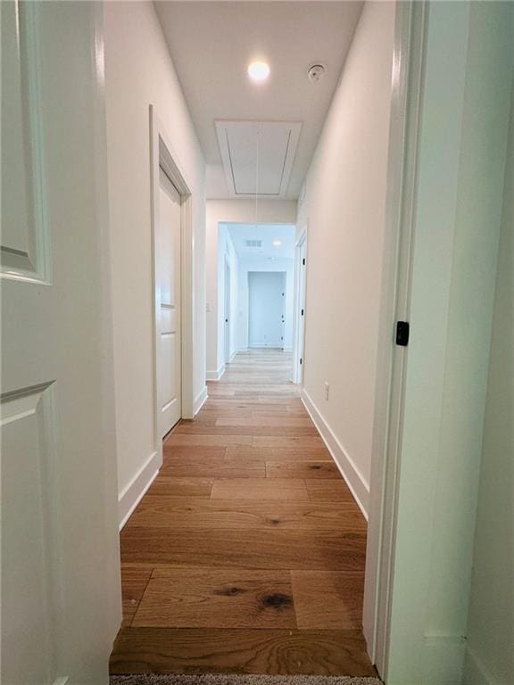 hall with baseboards, attic access, and light wood finished floors