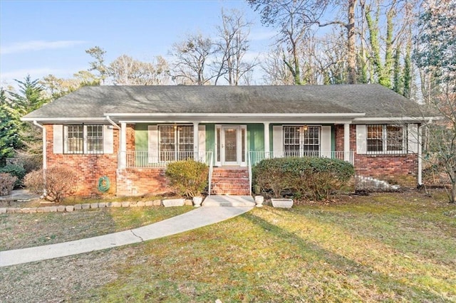 ranch-style home with a shingled roof, a front yard, covered porch, and brick siding