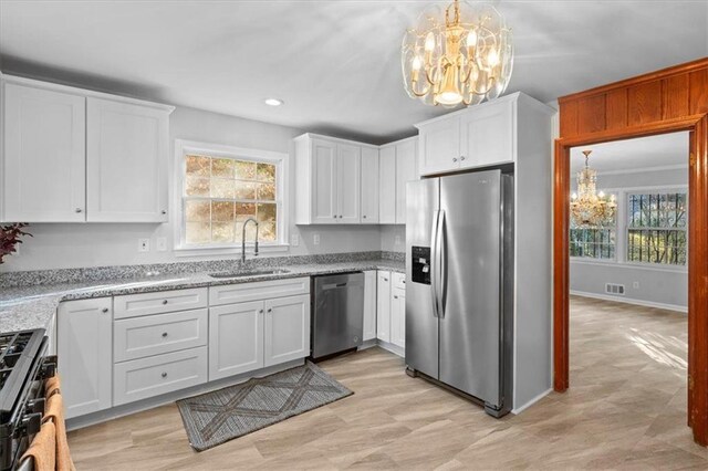 kitchen with appliances with stainless steel finishes, white cabinetry, a sink, a healthy amount of sunlight, and a chandelier