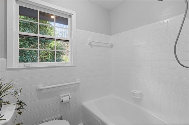 bathroom featuring shower / bathtub combination, toilet, and tile walls