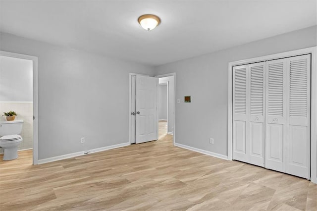 unfurnished bedroom with a closet, connected bathroom, light wood-style flooring, and baseboards