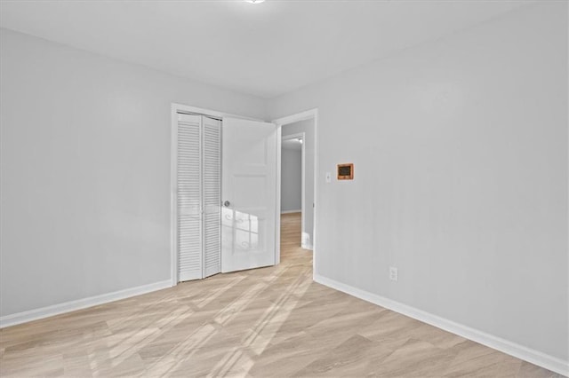 unfurnished bedroom with light wood-type flooring, a closet, and baseboards