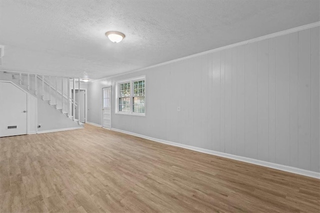 unfurnished living room featuring baseboards, ornamental molding, wood finished floors, stairs, and a textured ceiling