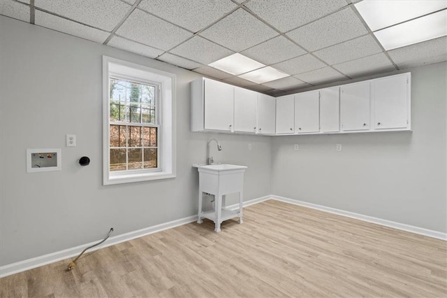 clothes washing area with light wood-style flooring, washer hookup, cabinet space, and baseboards