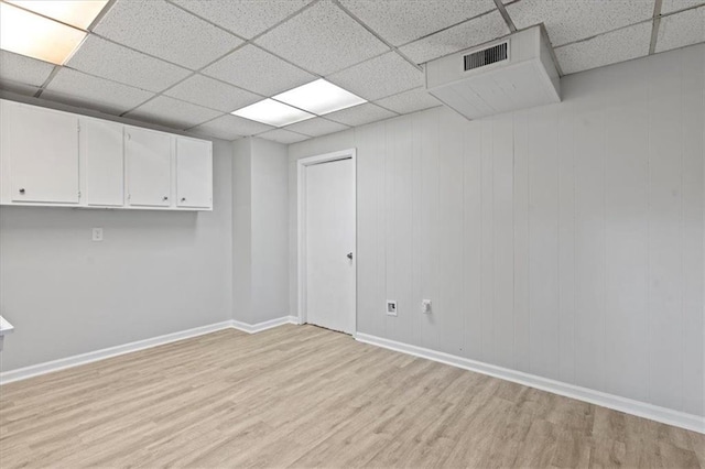 spare room with baseboards, visible vents, a drop ceiling, and light wood finished floors