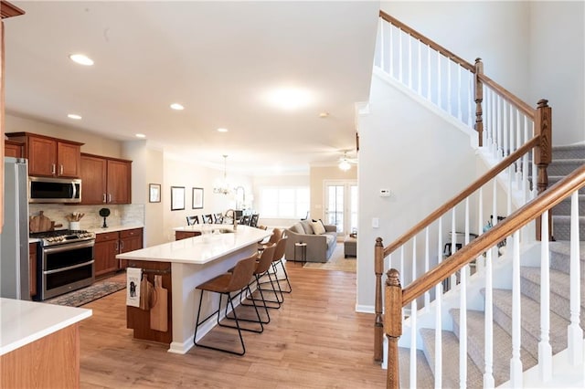 kitchen with sink, a breakfast bar area, appliances with stainless steel finishes, light hardwood / wood-style floors, and backsplash