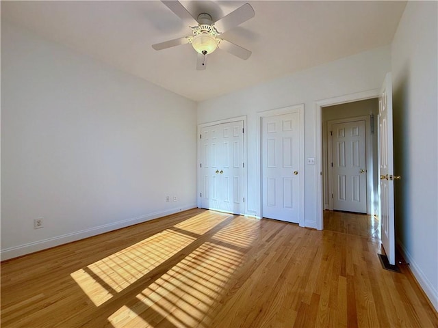 unfurnished bedroom featuring ceiling fan, two closets, and light wood-type flooring