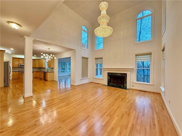 unfurnished living room with ornate columns, light wood-type flooring, a notable chandelier, a towering ceiling, and a premium fireplace