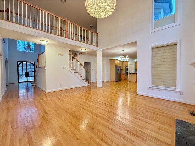 unfurnished living room with a towering ceiling, a chandelier, light hardwood / wood-style flooring, and ornate columns