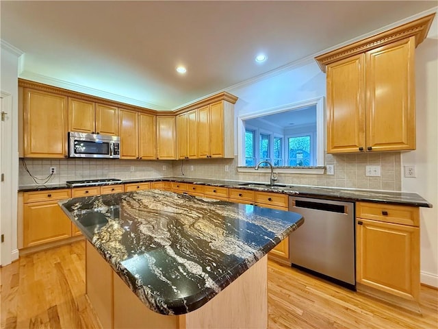 kitchen with sink, appliances with stainless steel finishes, dark stone countertops, a kitchen island, and light wood-type flooring