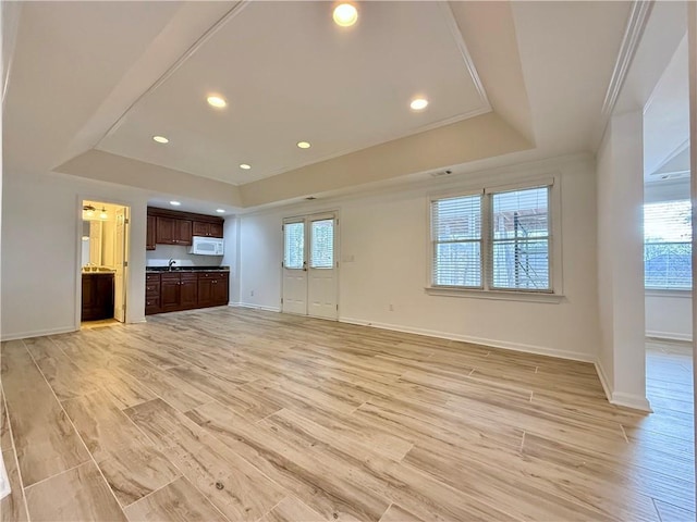 unfurnished living room with ornamental molding, light hardwood / wood-style floors, a raised ceiling, and a healthy amount of sunlight