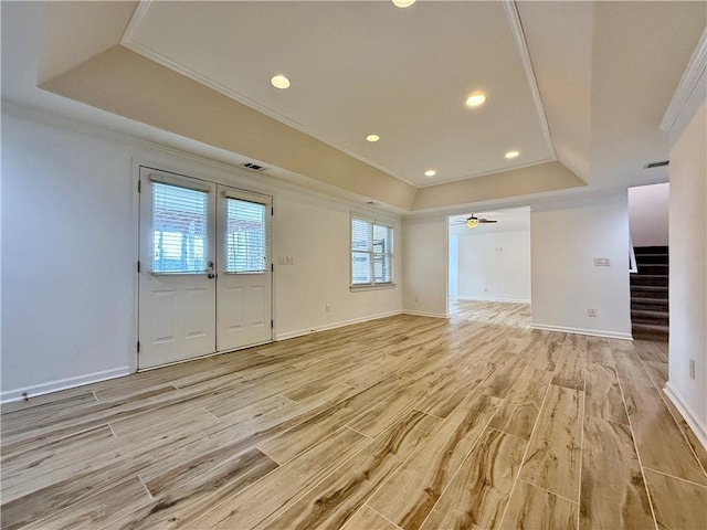 interior space with ceiling fan, ornamental molding, a raised ceiling, and light wood-type flooring