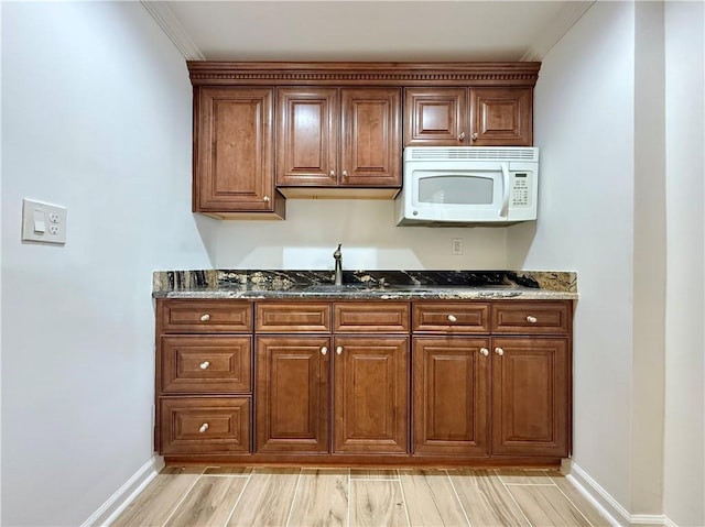 kitchen featuring ornamental molding, light wood-type flooring, and dark stone counters