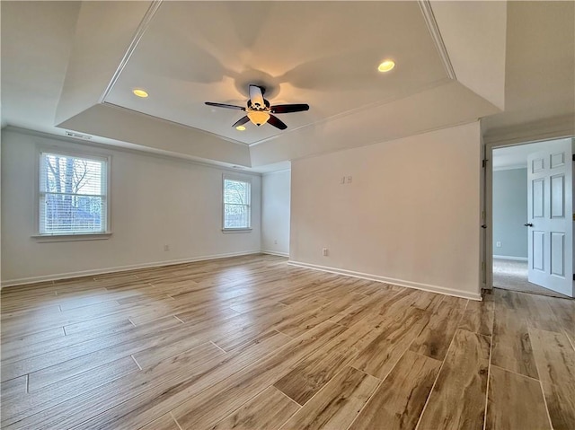 empty room with a tray ceiling, light hardwood / wood-style flooring, and ceiling fan