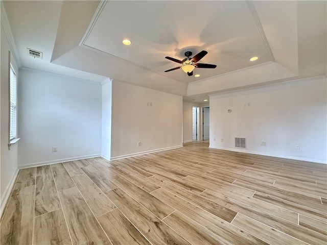 empty room with ceiling fan, crown molding, light hardwood / wood-style floors, and a tray ceiling