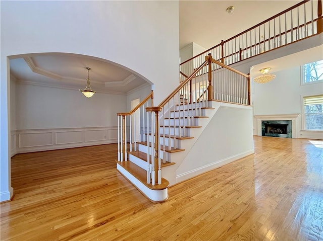 staircase with a towering ceiling, hardwood / wood-style floors, a high end fireplace, a tray ceiling, and crown molding