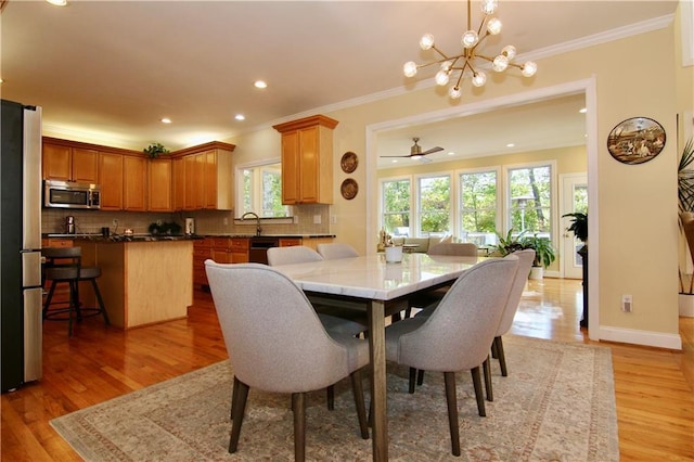 dining space with sink, ceiling fan with notable chandelier, ornamental molding, and light wood-type flooring