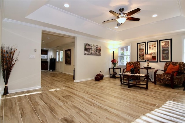 living area featuring a tray ceiling, light hardwood / wood-style flooring, ceiling fan, and plenty of natural light