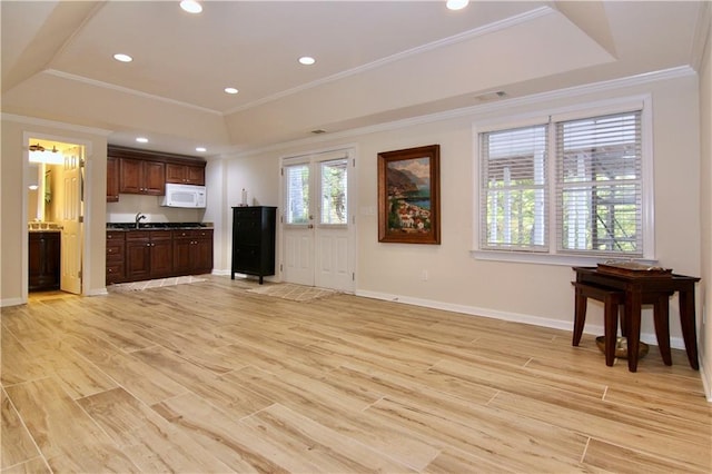 unfurnished living room featuring ornamental molding, sink, a raised ceiling, and light hardwood / wood-style floors