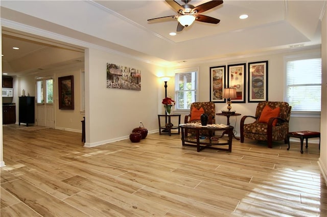 living area featuring crown molding, ceiling fan, a tray ceiling, and light hardwood / wood-style flooring