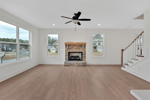 unfurnished living room with light wood-type flooring, baseboards, a wealth of natural light, and a stone fireplace