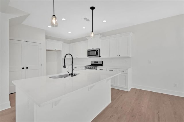 kitchen featuring a center island with sink, white cabinets, light wood-style flooring, appliances with stainless steel finishes, and a sink