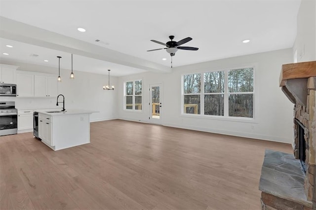 unfurnished living room with a wealth of natural light, light wood-type flooring, a sink, and a stone fireplace