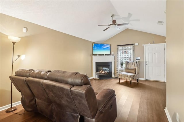 living room with a glass covered fireplace, ceiling fan, wood finished floors, and vaulted ceiling