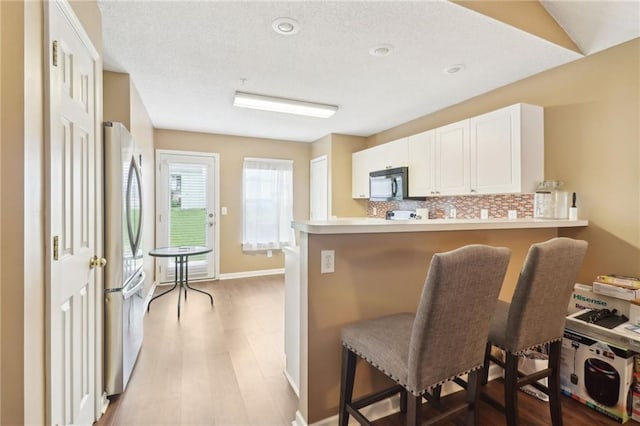 kitchen with a breakfast bar area, backsplash, black microwave, freestanding refrigerator, and a peninsula
