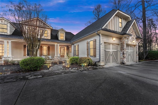 view of front facade with aphalt driveway, stone siding, a porch, board and batten siding, and a shingled roof