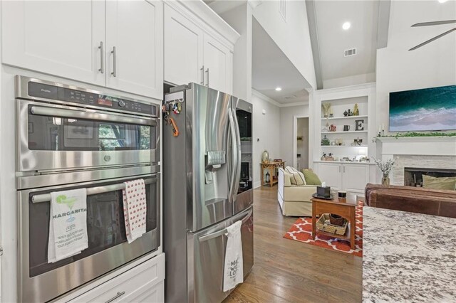 kitchen with dark wood-type flooring, white cabinetry, stainless steel appliances, light stone countertops, and ceiling fan