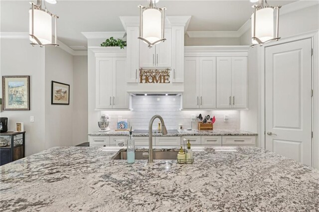 kitchen with ornamental molding, pendant lighting, light stone counters, and white cabinets