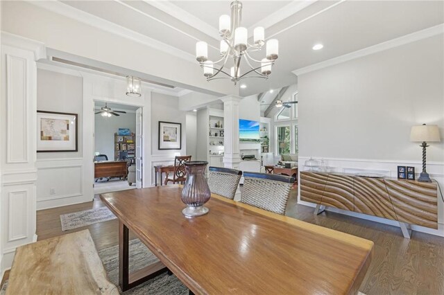 dining area featuring ceiling fan with notable chandelier, a fireplace, ornate columns, ornamental molding, and hardwood / wood-style floors