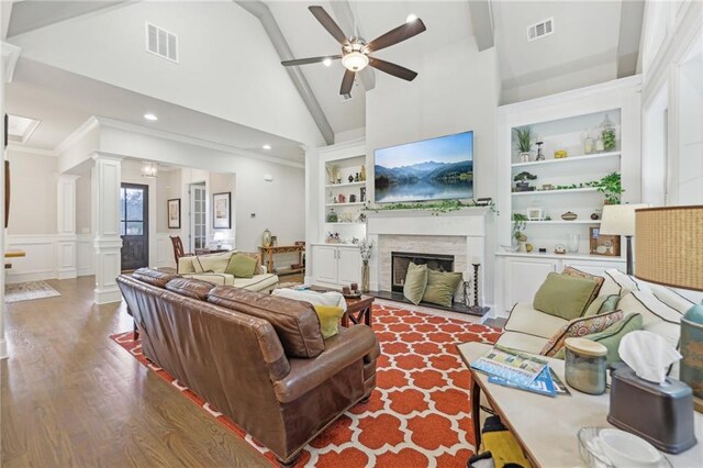 living room featuring built in shelves, high vaulted ceiling, wood-type flooring, ceiling fan, and decorative columns