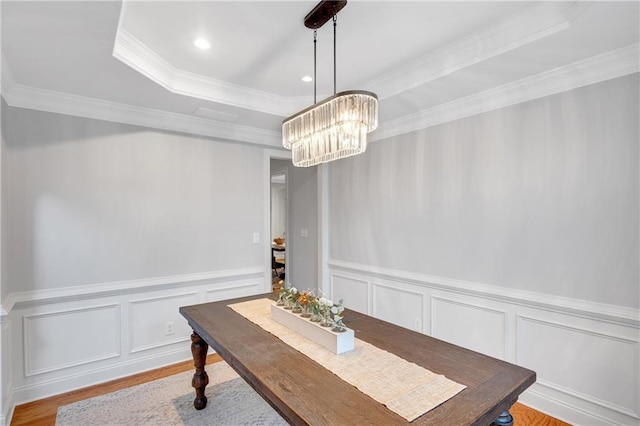 dining area with an inviting chandelier, ornamental molding, a raised ceiling, and light hardwood / wood-style flooring