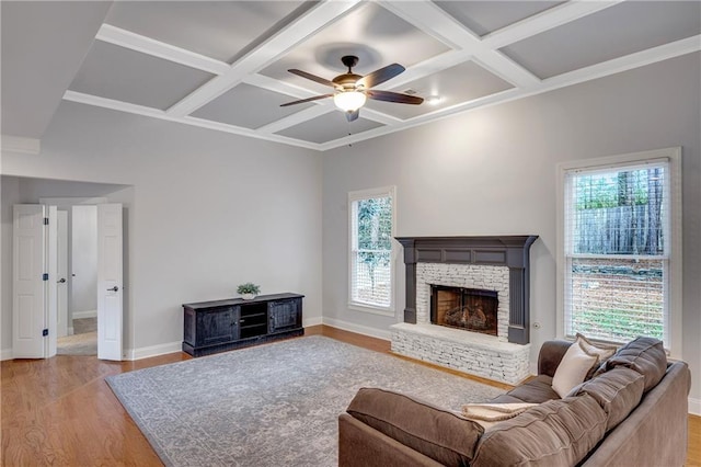 living room with coffered ceiling, a stone fireplace, beam ceiling, and light wood-type flooring