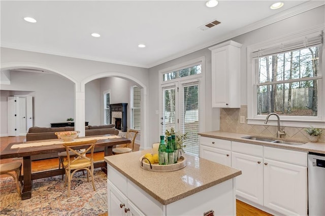 kitchen with sink, dishwasher, a kitchen island, white cabinets, and backsplash