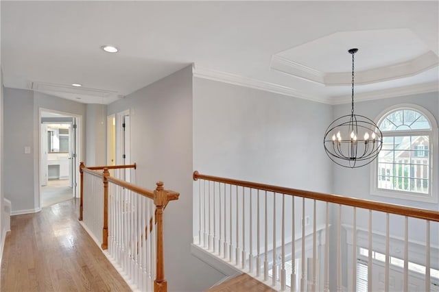 corridor featuring crown molding, a raised ceiling, light hardwood / wood-style flooring, and a notable chandelier