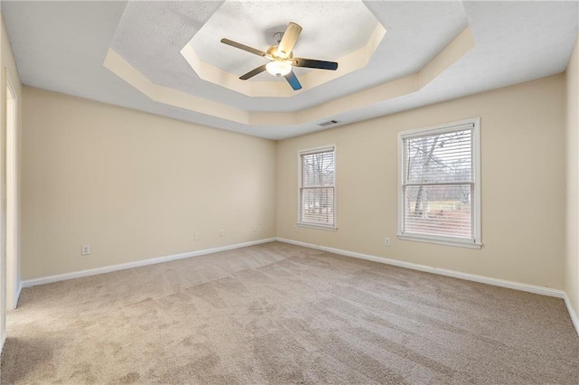 carpeted spare room with a tray ceiling and ceiling fan