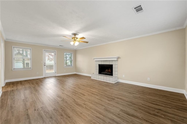 unfurnished living room featuring ceiling fan, wood-type flooring, ornamental molding, and a tiled fireplace